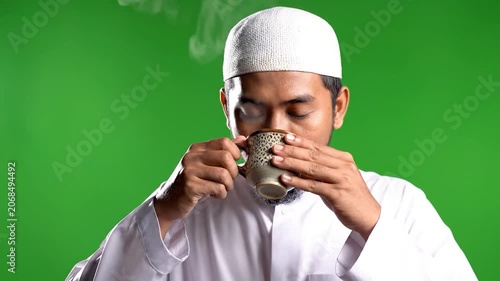 A smiling Muslim man holds a steaming cup of coffee