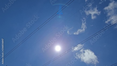 Clouds sweep fast in a time-lapse, shifting between direct rays and diffused light. As they mask the sun behind overhead power lines in the blue sky, changing light creates a dramatic pulsing effect.