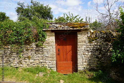Door with a door knocker in an old stone wall overgrown with plants. Blue sky, Châteauneuf, Burgundy, France. June.