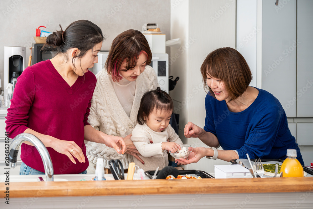 Fototapeta premium Group of happy Asian mothers cooking pizza with a curious toddler at a modern kitchen counter