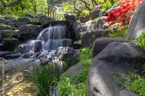 Long exposure of a beautiful small waterfall cascading over rocks in a lush green garden.