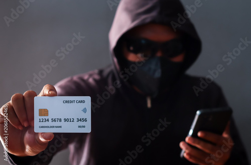 Obraz na płótnie Anonymous cybercriminal using a smartphone and credit card in a dark environment, representing online fraud, phishing attacks, identity theft, financial scams, and cybersecurity threats