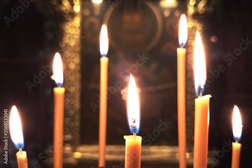 Burning candles stand in a church against the backdrop of an icon.