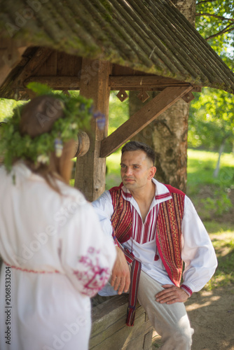Photography Young romantic slavic couple in traditional embroidered clothes talking near vil