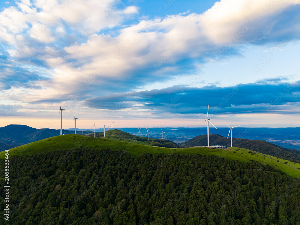 Obraz premium Wind turbines stand on a green hill under a cloudy sky in a rural area during late afternoon