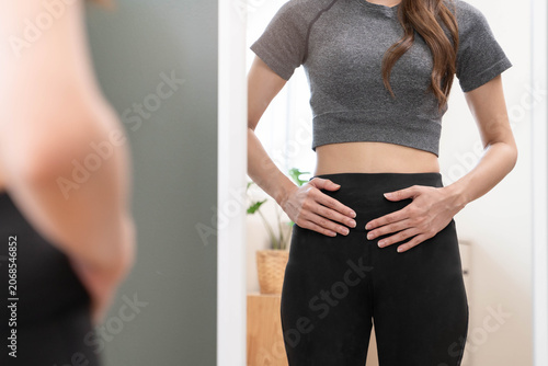 Fotografie Fit woman checking her slim waist in mirror at home, healthy lifestyle concept