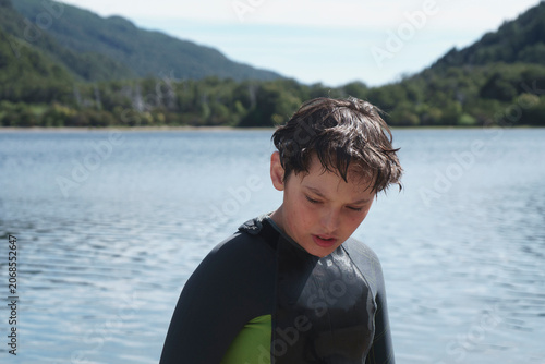 Thoughtful boy wearing a wetsuit by a lake
