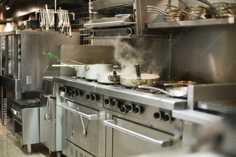 Obraz premium Stainless steel commercial kitchen with pots and pans steaming on the