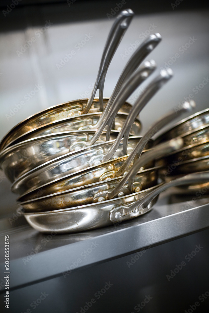 Fototapeta premium Stack of stainless steel frying pans on a kitchen shelf