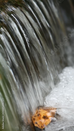 A close-up view of a flowing waterfall with smooth water cascading over rocks. The scene captures the natural beauty and tranquility of a stream.