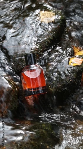 Fragrance bottle filled with amber perfume displayed on wet stone under stream flow. Minimalist nature-inspired concept for beauty branding and editorial campaigns