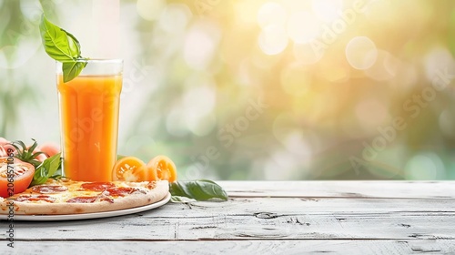 A refreshing orange drink, pizza, and tomatoes sit on a white table, blurred green backdrop