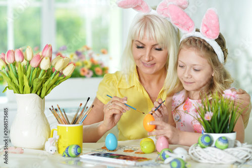 Mother with daughter wearing rabbit ears decorating Easter eggs