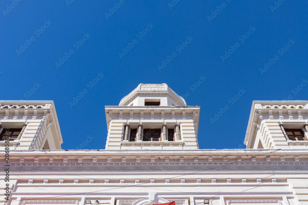 Fototapeta premium Historic White Neoclassical Facade with Tower Elements Under Deep Blue Sky