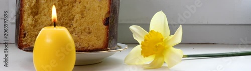 Easter cake burning candle and daffodil symbolizing spring renewal and celebration on a tabletop.