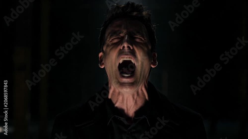 Portrait of a man screaming in darkness expressing intense emotion