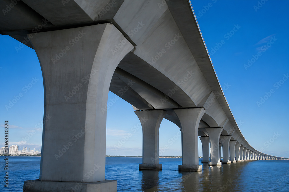 Naklejka premium A large concrete bridge spans over a body of water under a clear blue sky.