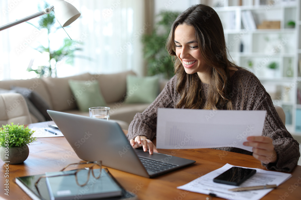 Fototapeta premium Happy teleworker comparing paper document online working at home