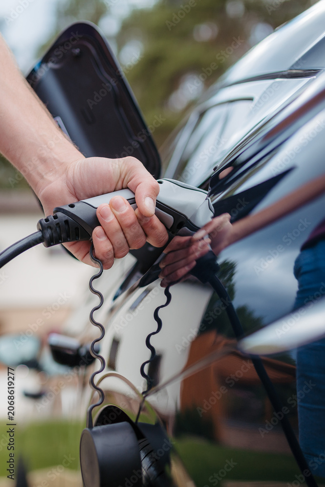 Naklejka premium Man holding power supply cable at electric vehicle charging station.