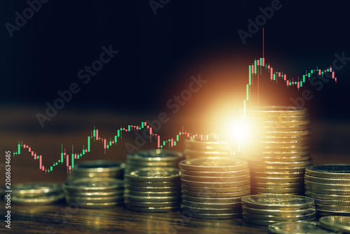 Stacked coins with glowing light and candlestick chart illustrating investment growth, wealth management, financial success, stock market trading, savings strategy, and long term economic growth.