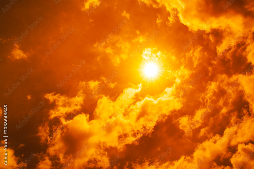 Obraz premium Dramatic blazing sun shining through fiery orange clouds during an extreme heatwave, global boiling and climate crisis concept, hot summer weather background.