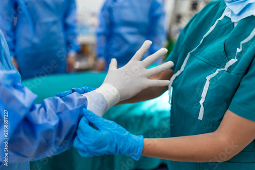 Sterile surgical nurse assists a surgeon in putting on sterile gloves in a modern hospital operating room, ensuring strict hygiene protocols are followed before a medical procedure begins. 