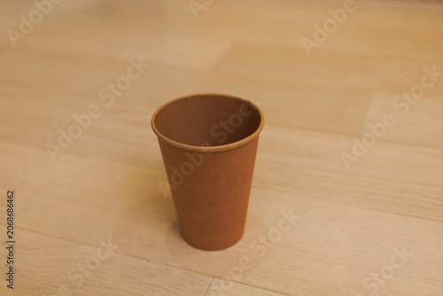 A brown paper cup stands alone on a wooden floor in a calm indoor area