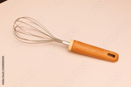 A wooden-handled whisk with metal wires sits on a smooth surface, ready for cooking