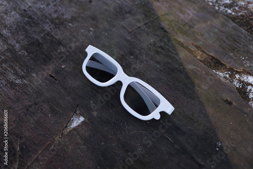 White sunglasses lie on a wooden surface with some snow present in the surrounding area