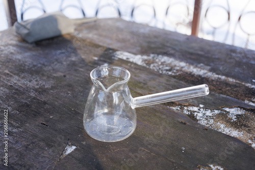 A glass coffee pot rests on a wooden table in a snowy setting