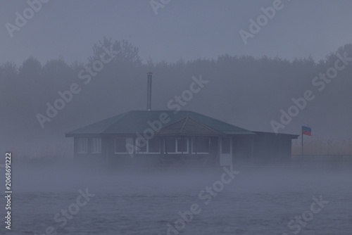 Wooden birdwatching and fishing cabin on wooden stilts shrouded in thick morning fog on Lake Chaika at Curonian Spit