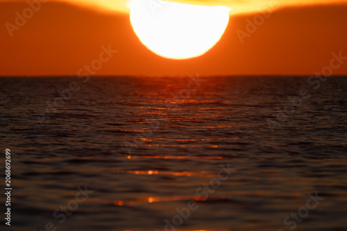 Extreme close-up of a massive bright sun dipping below the sea horizon during a spectacular golden sunset