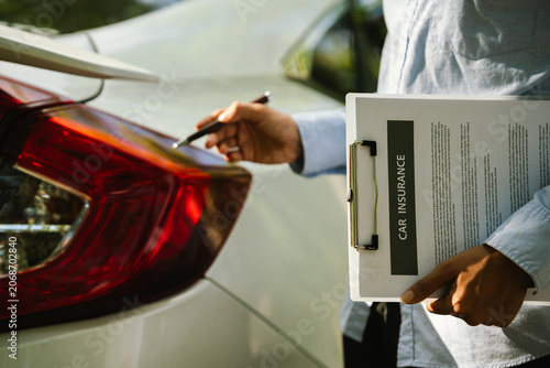 Photography Close-up of an insurance agent inspecting a car and holding a car insurance document during a vehicle assessment, representing auto insurance claims, inspection, and customer service