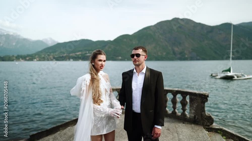 Elegant couple walks on a stone balustrade overlooking Lake Como in Italy