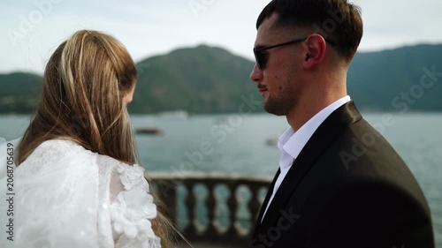 Stylish couple poses by Lake Como Italy with mountains and sailboat in background
