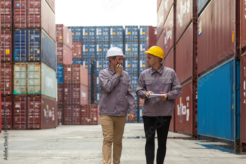 Two shipping company workers at commercial dock site. Group of male worker control loading container box from cargo freight ship for import export.