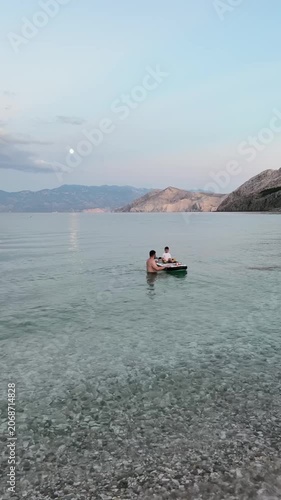 father with toddler son on puddleboard in calm sea at dusk