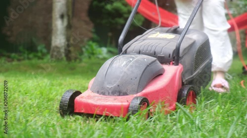 Person mowing backyard lawn near red hammock