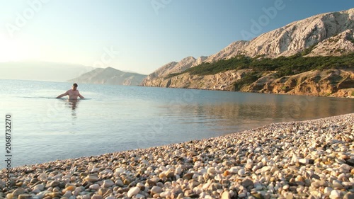 Calm sea sunset with rocky shore and swimmer