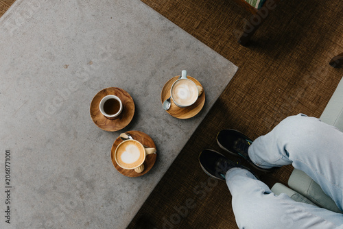 Overhead shot of two cups of hot beverages in coffee shop with persons feet
