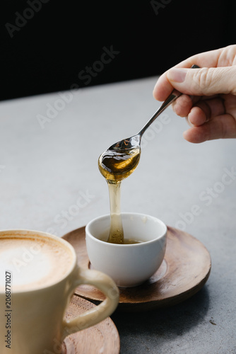 Teaspoon with honey dripping into cup