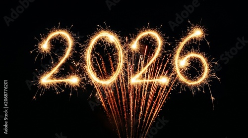 2026 sparkler text written in glowing light against a dark night background with festive golden firework explosions for a happy new year celebration greeting card