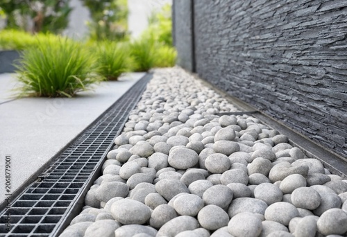 Modern French drain system with gravel stones and protective grate ensuring efficient water drainage, outdoor surface protection, and durable architectural exterior landscaping solution.
