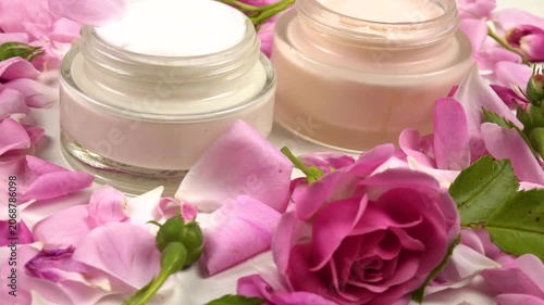 Jars with face cream with use rose essential oil, fresh pink roses are on a white table, background, side view