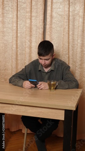 Teenager focused on playing a handheld gaming console while sitting at a table at home, with a cup of tea nearby.