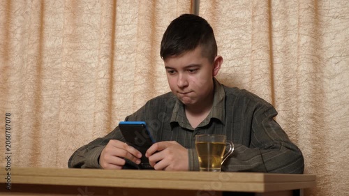 Teenager focused on playing a handheld gaming console while sitting at a table at home, with a cup of tea nearby.