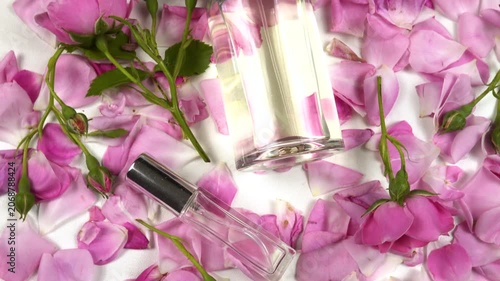 Bottles with perfumes and eau de toilette with use rose essential oil, fresh pink roses are on a white table, top view