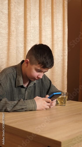 Teenager focused on playing a handheld gaming console while sitting at a table at home, with a cup of tea nearby.
