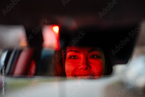 Bild auf Leinwand Woman smiling in car rear view mirror at night