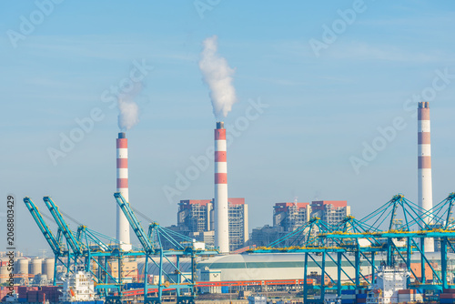 Industrial port and power plant with smokestacks in Shanghai, China. Cargo handling equipment and energy production facilities illustrate logistics, electricity generation, heavy industry